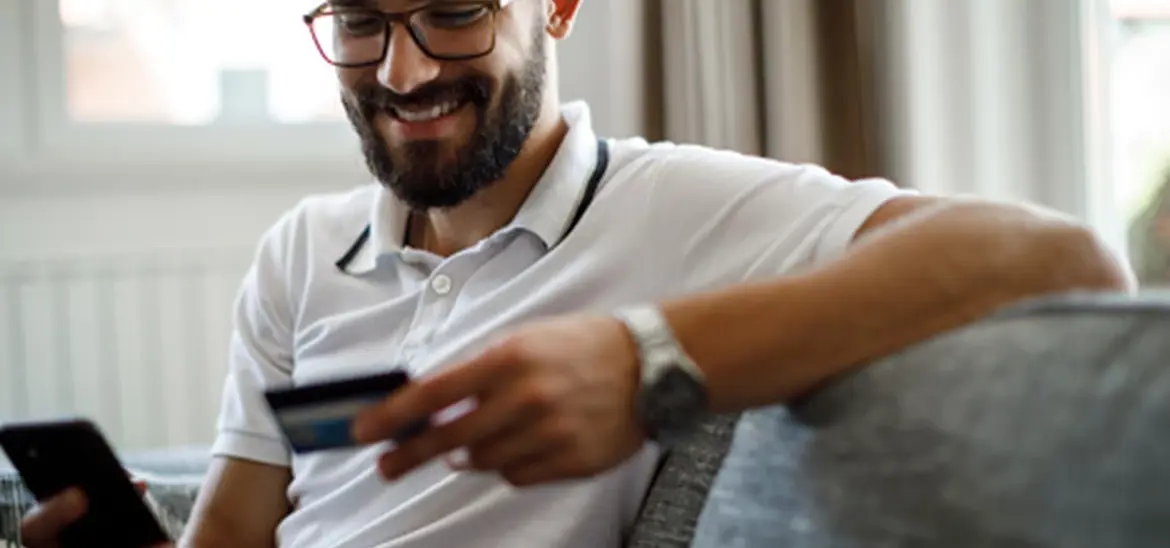 A man smiling with a cell phone in one hand while holding a credit card in another hand