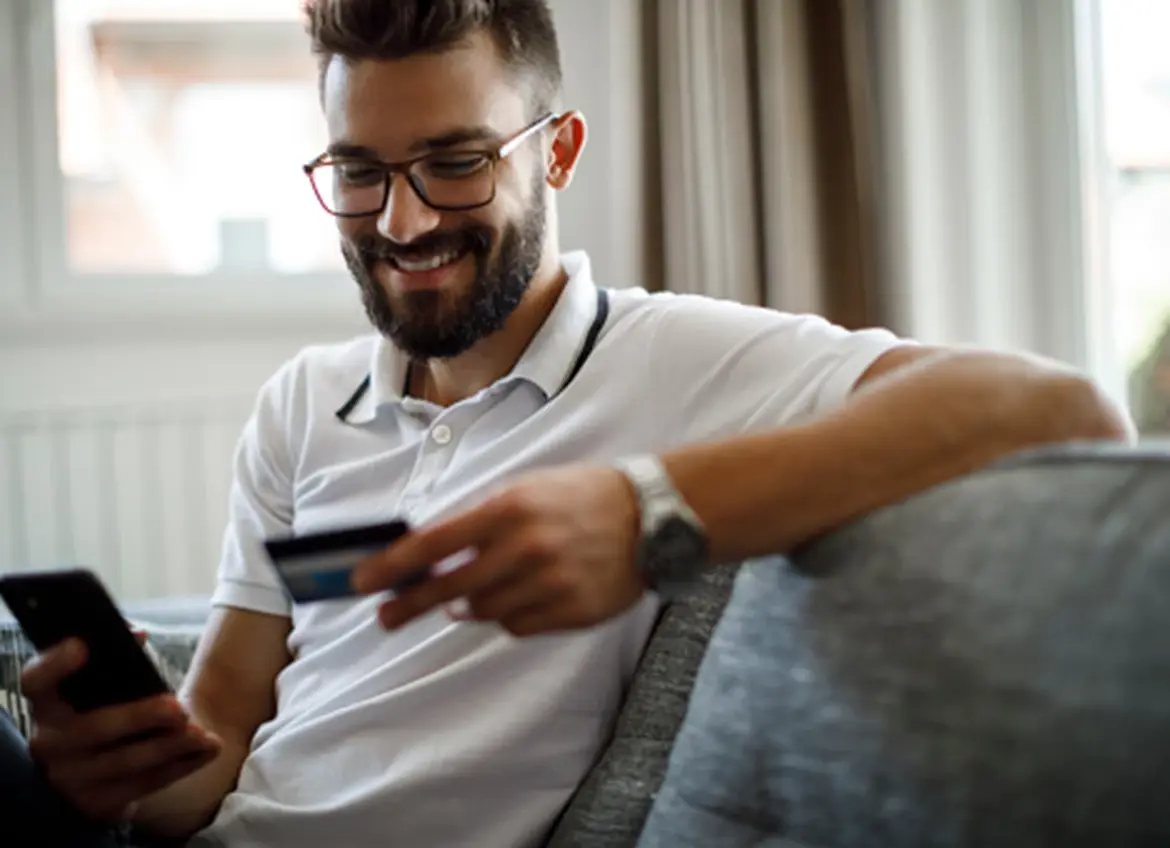 A man smiling with a cell phone in one hand while holding a credit card in another hand