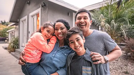 A happy family with parents and two kids smiling in front of their home