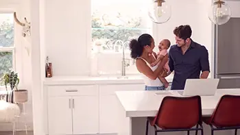 A happy couple is standing in the kitchen, holding and looking at their baby