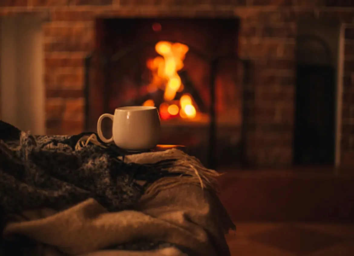 A cup of warm tea with fire lit in the fireplace