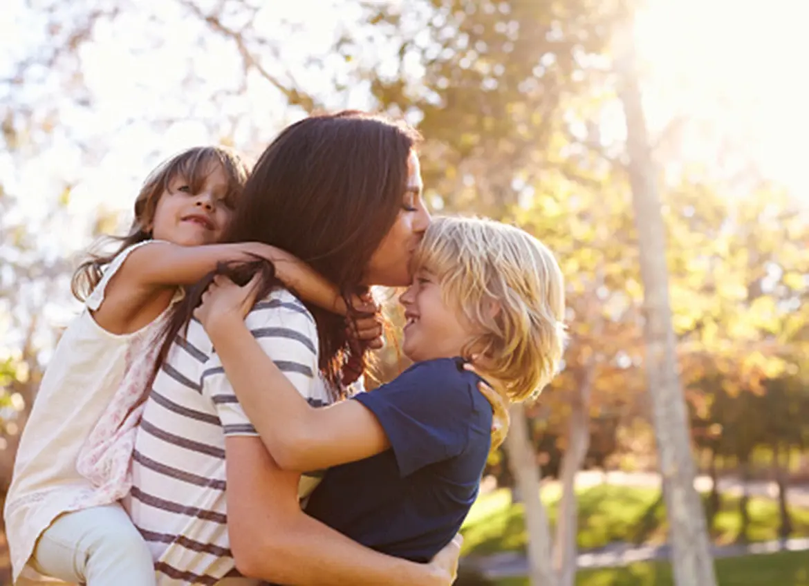 A woman sharing a loving hug with two children while enjoying a sunny day in the park