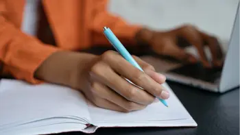 A woman writing on paper while using her laptop