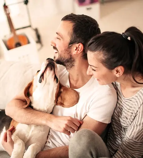 A couple cuddling with their dog and smiling