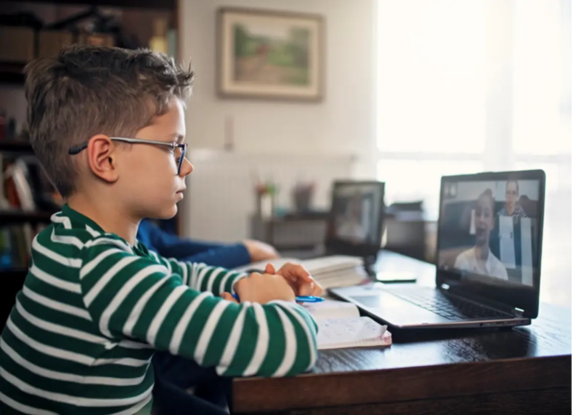 A boy watching a virtual meeting with his notebook opened