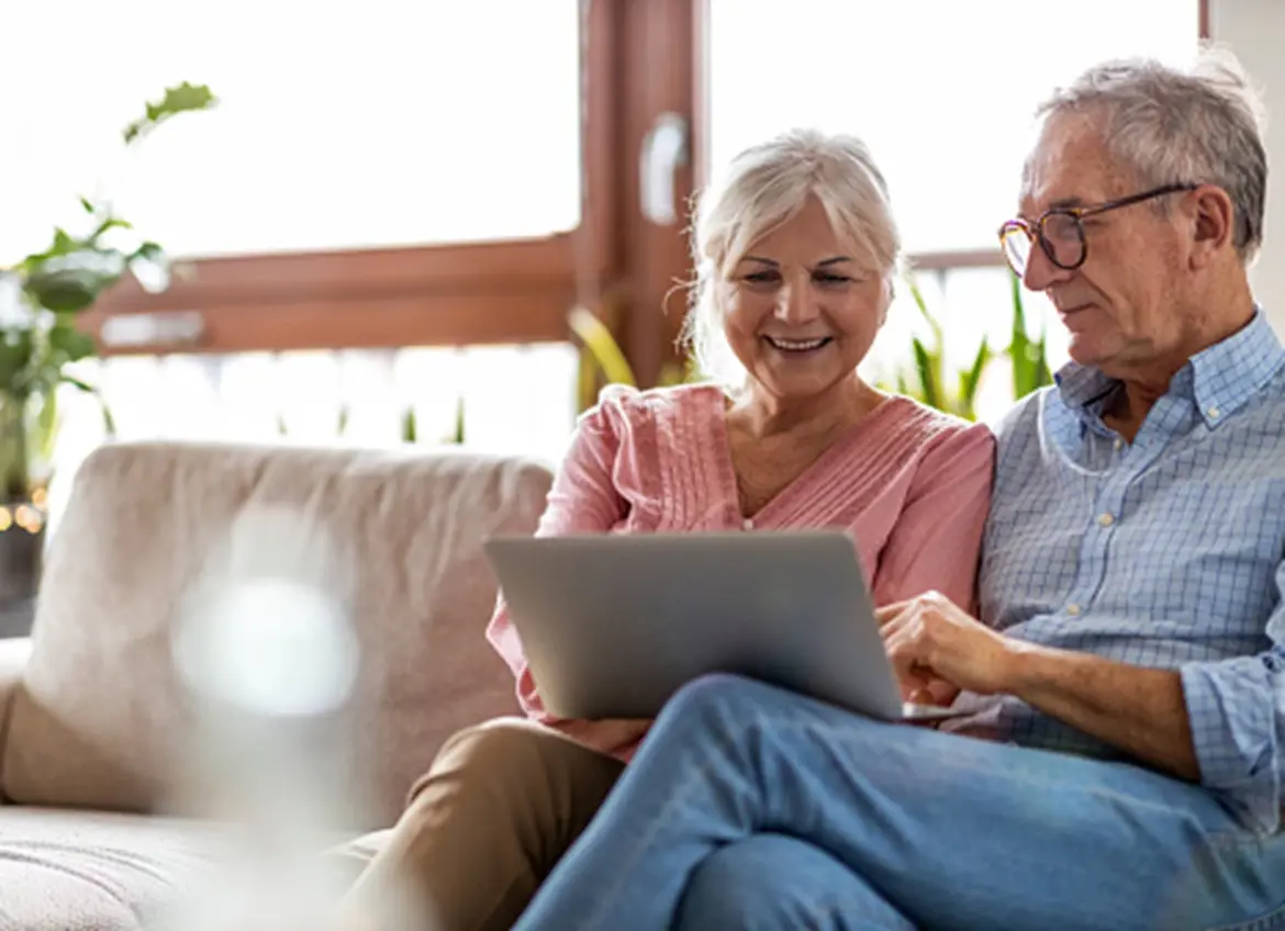 A senior couple sitting on a couch and looking at a laptop screen together