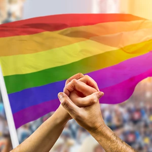 two hands holding together in front of Pride flag