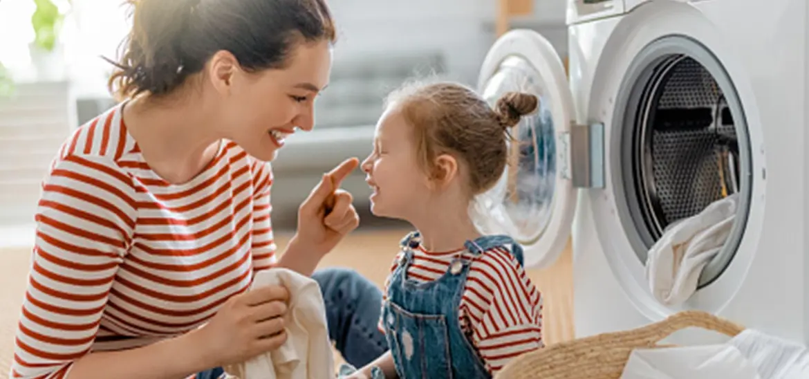 A mom and a daughter smiling while folding laundry together