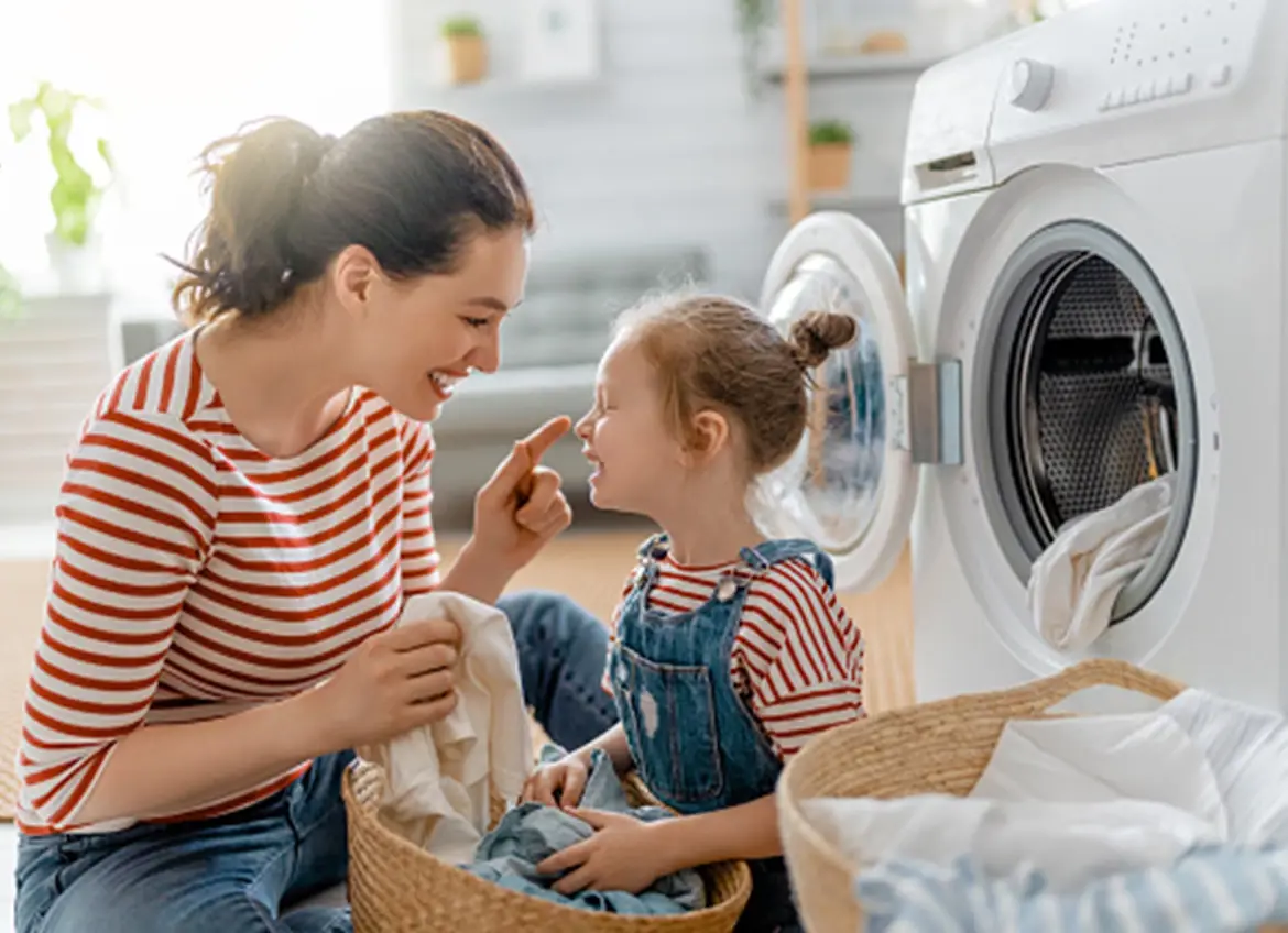 A mom and a daughter smiling while folding laundry together