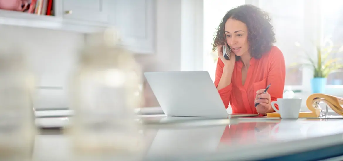 Woman talking over phone while looking at a laptop