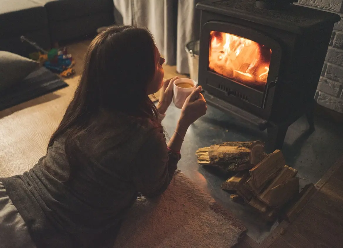 Woman is gazing at fireplace while lying on her belly holding a cup of tea