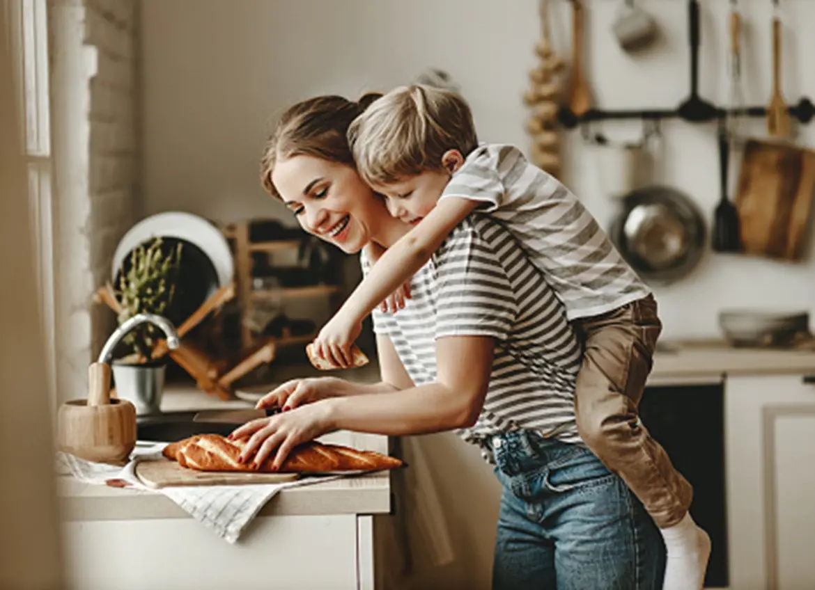 A smiling mom slicing bread while carrying her son piggyback